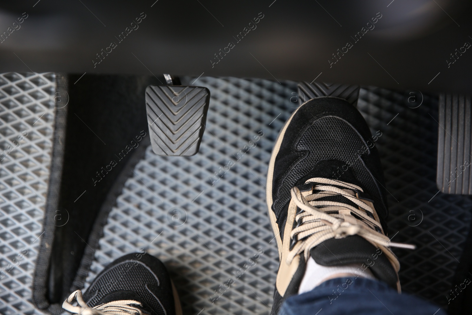 Photo of Man in sneakers pushing on pedal of car brake, closeup