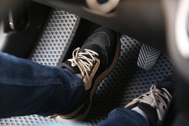 Photo of Man in sneakers pushing on pedal of car brake, closeup