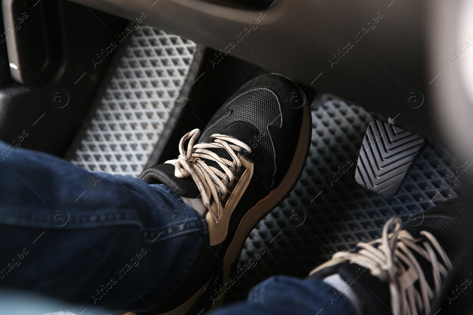 Photo of Man in sneakers pushing on pedal of car brake, closeup