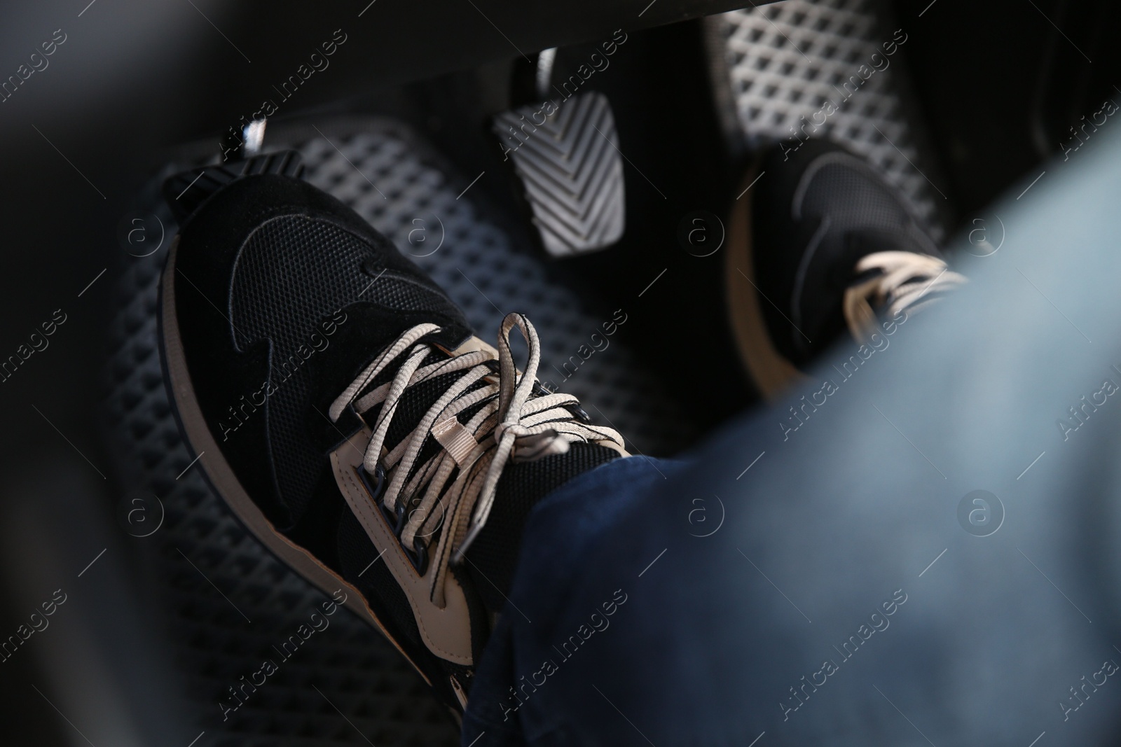 Photo of Man in sneakers pushing on pedal of car brake, closeup