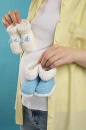 Expecting twins. Pregnant woman holding two pairs of baby shoes on light blue background, closeup