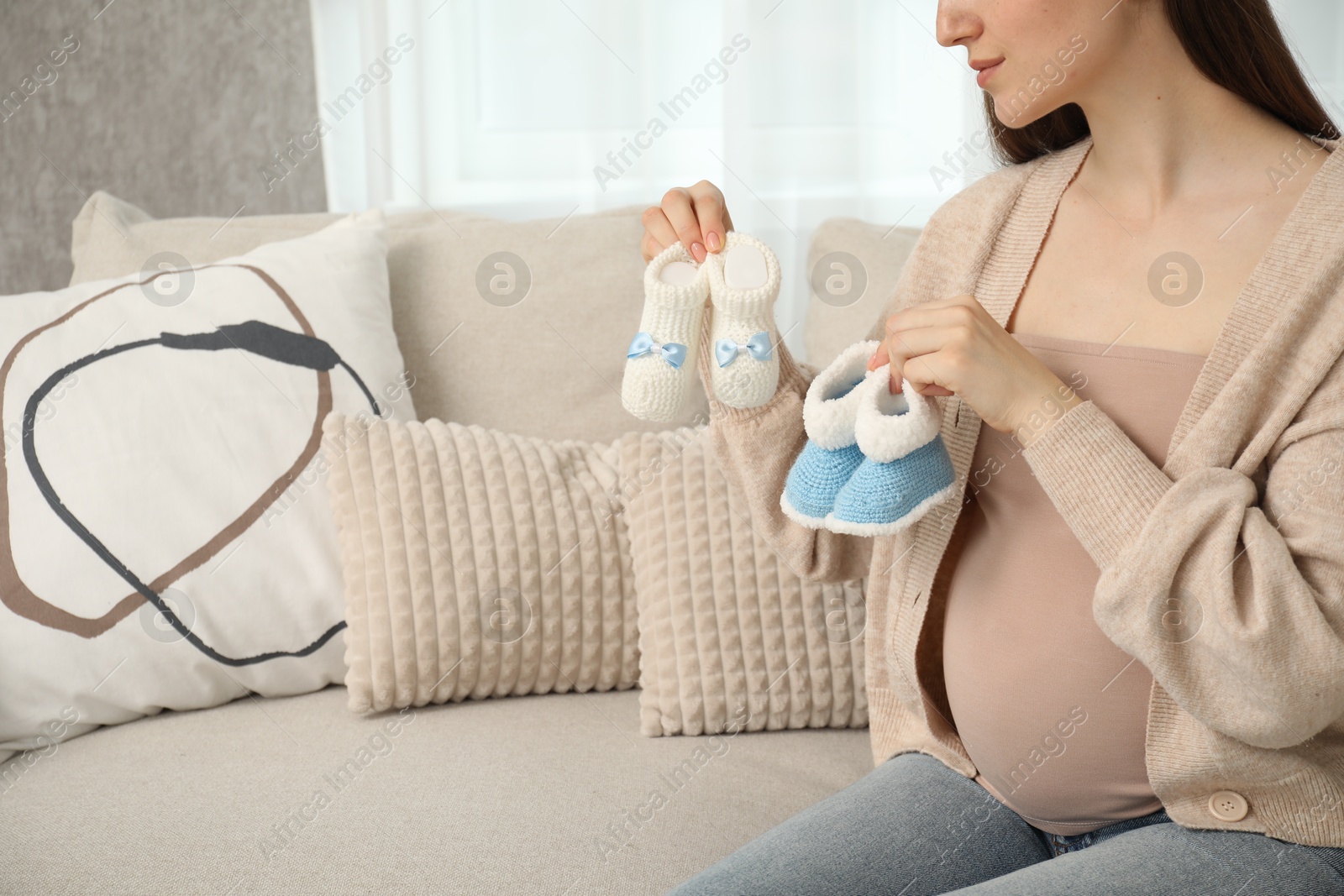 Photo of Expecting twins. Pregnant woman holding two pairs of shoes at home, closeup. Space for text