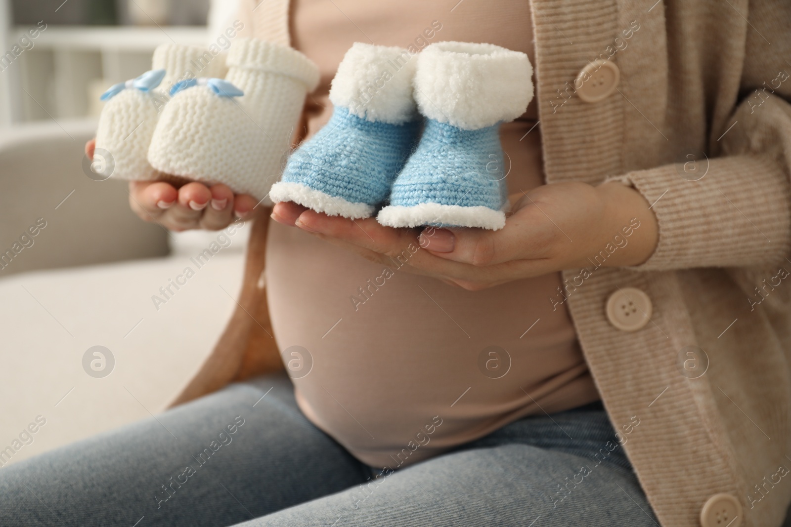 Photo of Expecting twins. Pregnant woman holding two pairs of shoes at home, closeup