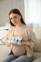 Expecting twins. Pregnant woman holding two pairs of shoes at home