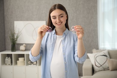 Expecting twins. Pregnant woman holding two pacifiers at home