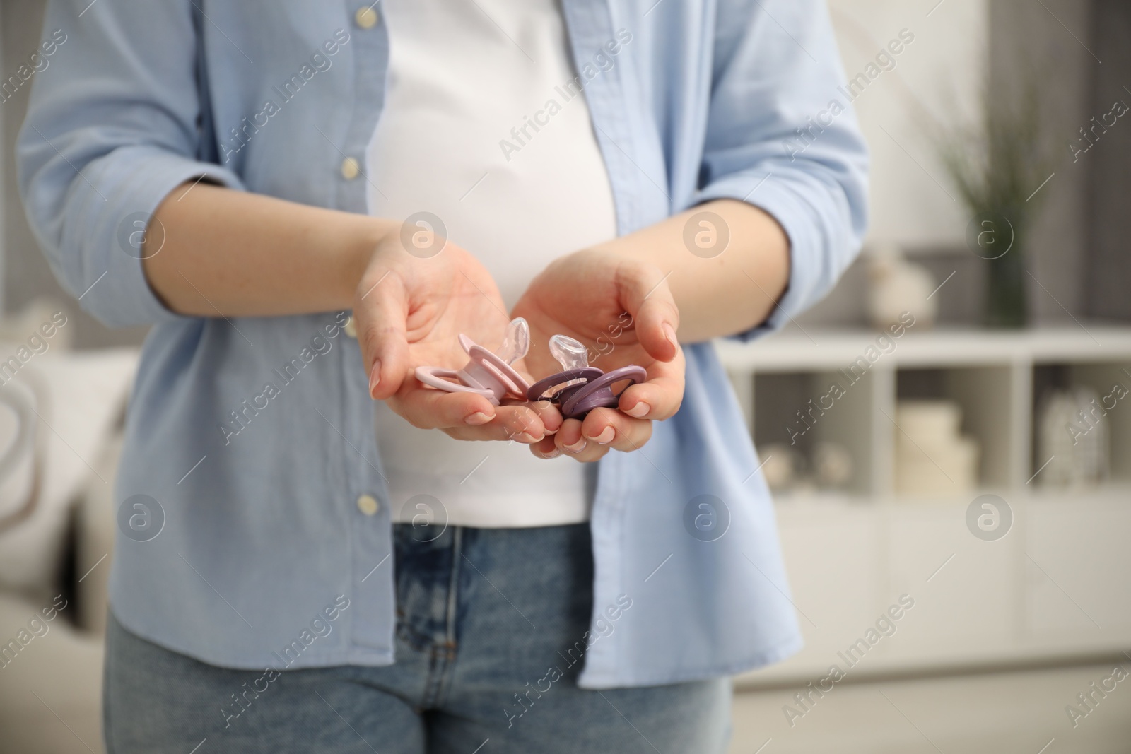 Photo of Expecting twins. Pregnant woman holding two pacifiers at home, closeup