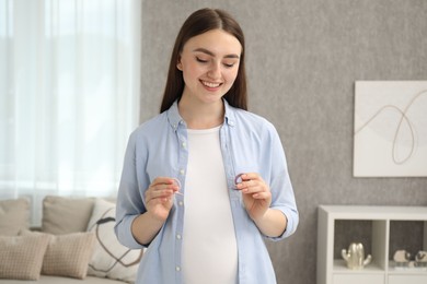 Expecting twins. Pregnant woman holding two pacifiers at home