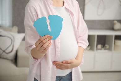 Photo of Expecting twins. Pregnant woman holding two paper cutouts of feet at home, closeup