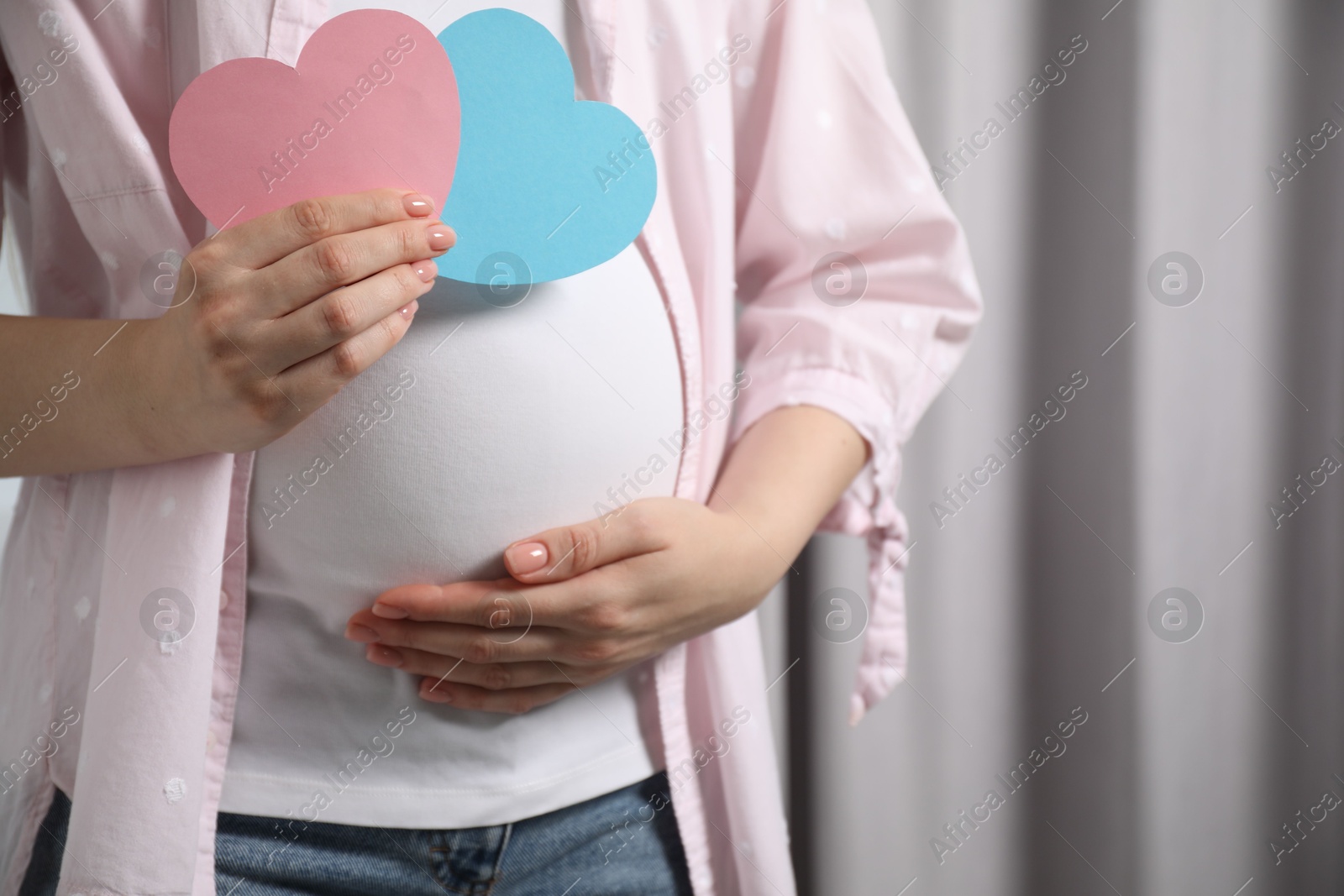 Photo of Expecting twins. Pregnant woman holding two paper cutouts of hearts at home, closeup. Space for text