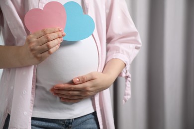 Expecting twins. Pregnant woman holding two paper cutouts of hearts at home, closeup. Space for text