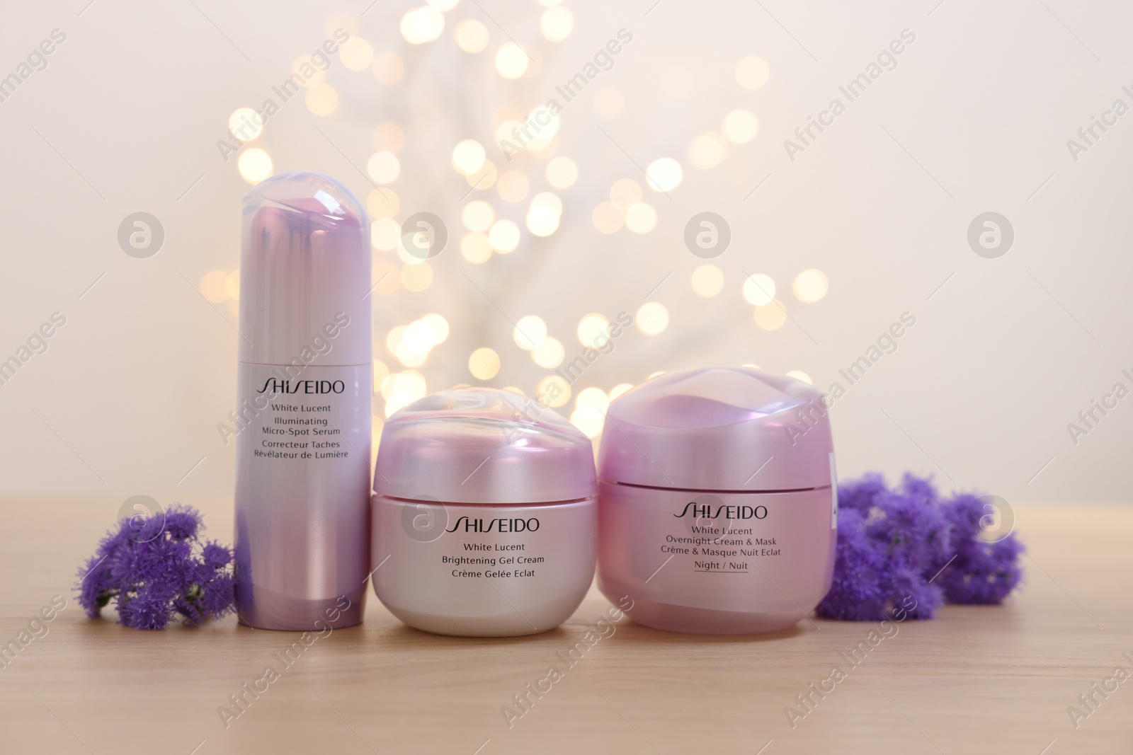 Photo of Leiden, Netherlands - June 11, 2024: Shiseido care cosmetic products and ageratum flowers on wooden table against light background with blurred lights