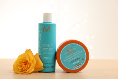 Photo of Leiden, Netherlands - June 11, 2024: Moroccanoil hair care cosmetic products and yellow rose flower on wooden table against light background