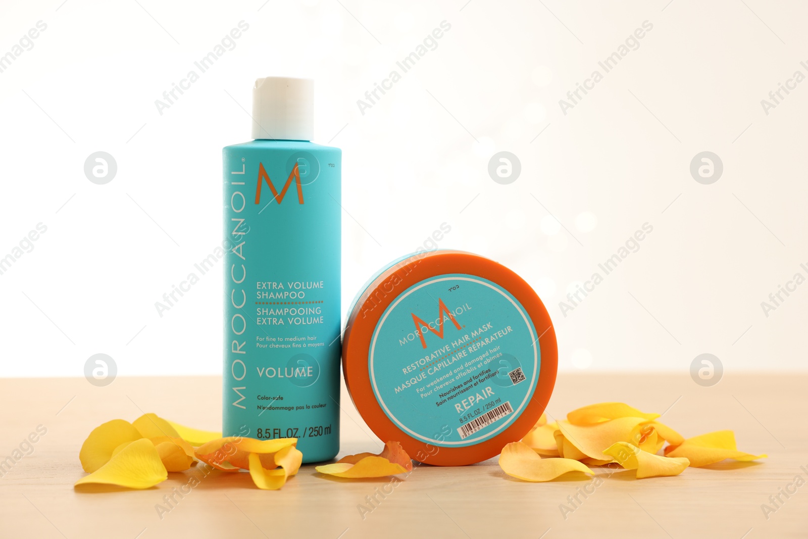 Photo of Leiden, Netherlands - June 11, 2024: Moroccanoil hair care cosmetic products and yellow petals on wooden table against light background