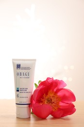 Photo of Leiden, Netherlands - June 11, 2024: Tube of Obagi sunscreen and peony flower on wooden table against light background, space for text