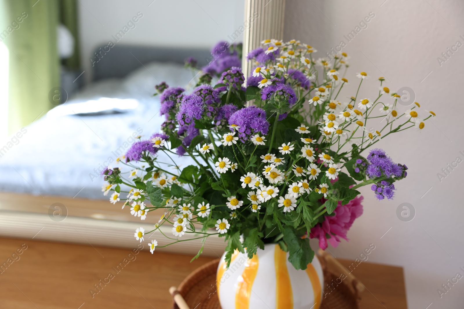 Photo of Beautiful flowers in vase and mirror on wooden table indoors