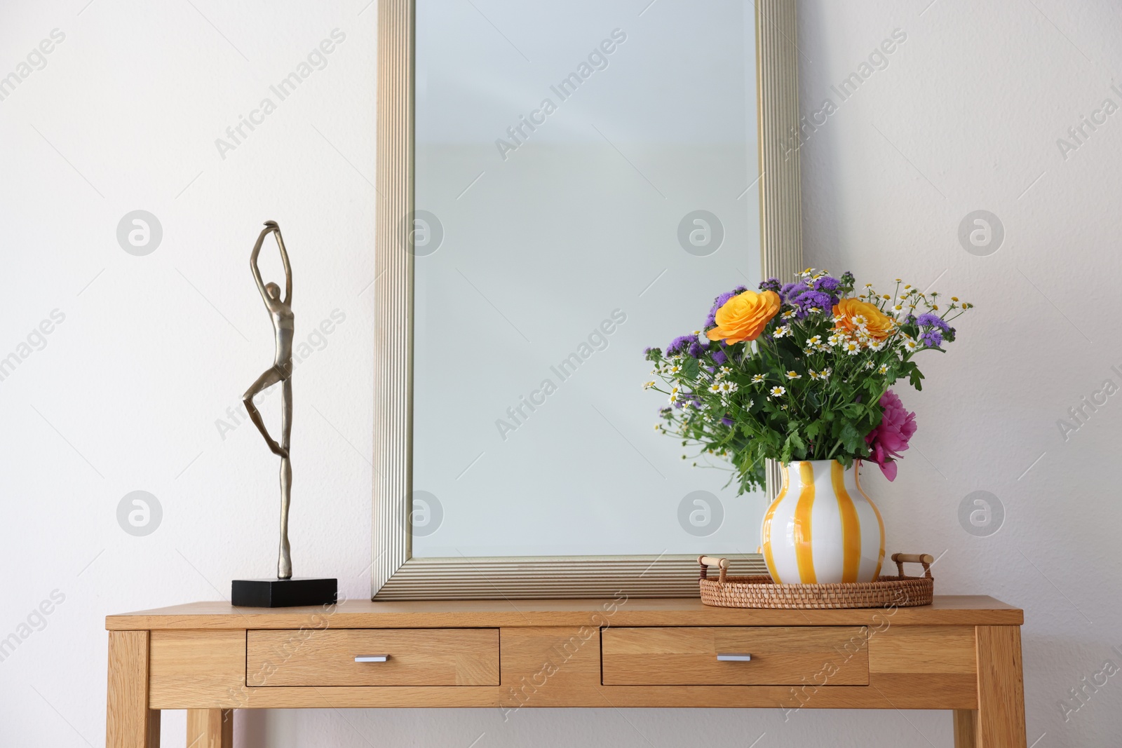 Photo of Beautiful flowers in vase and mirror on wooden table indoors