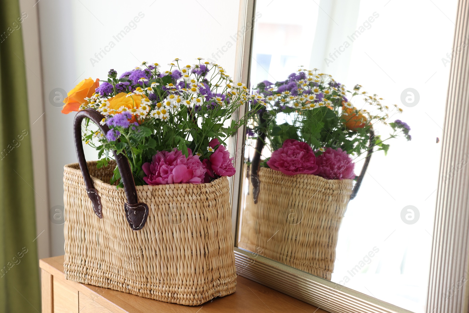 Photo of Wicker basket with beautiful flowers on wooden table indoors