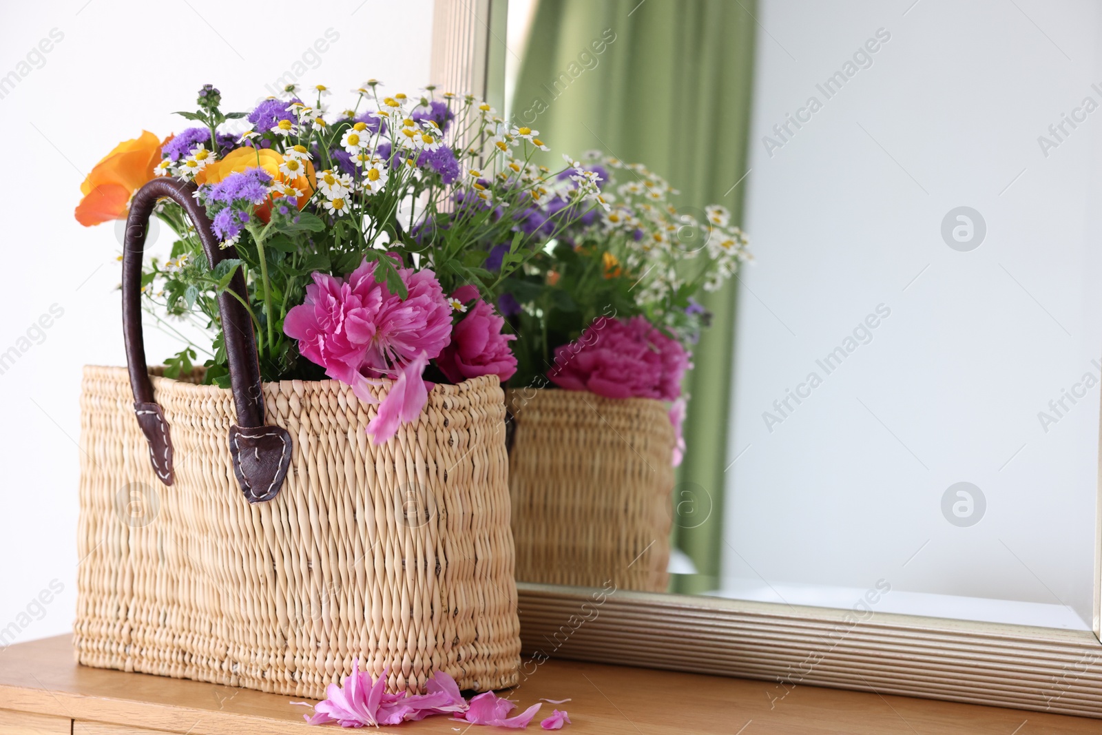 Photo of Wicker basket with beautiful flowers on wooden table indoors, space for text