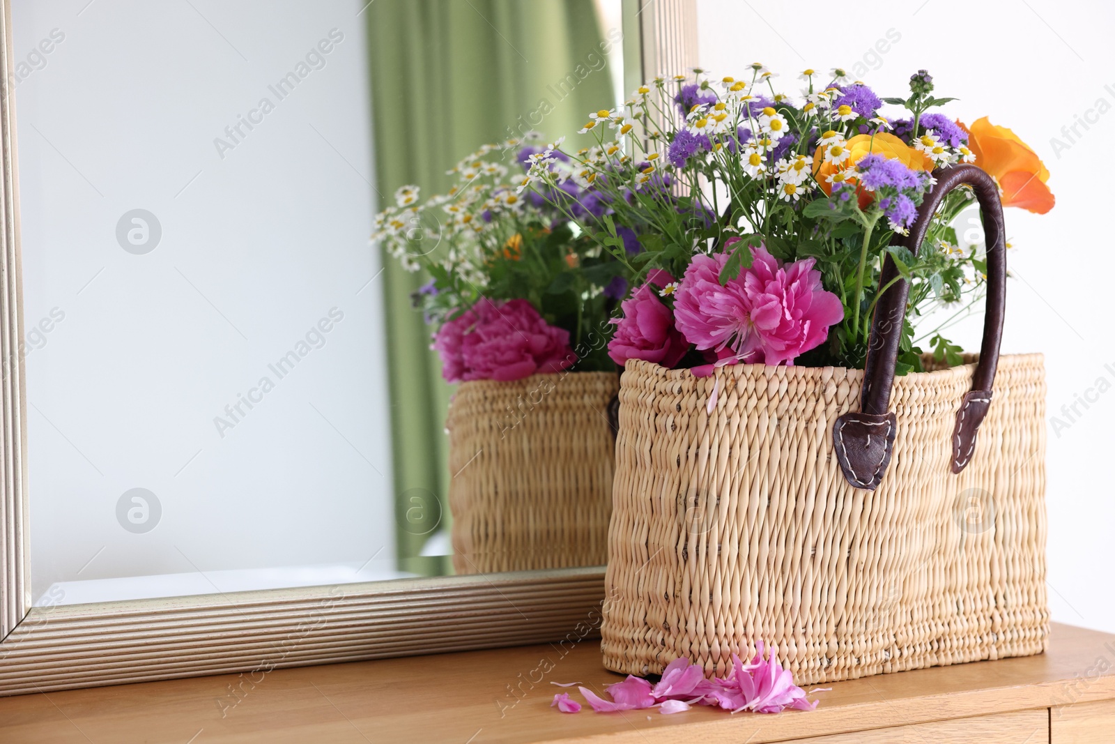 Photo of Wicker basket with beautiful flowers on wooden table indoors, space for text