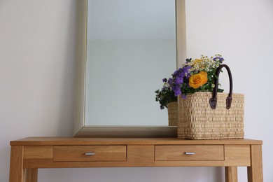 Photo of Wicker basket with beautiful flowers on wooden table indoors, space for text