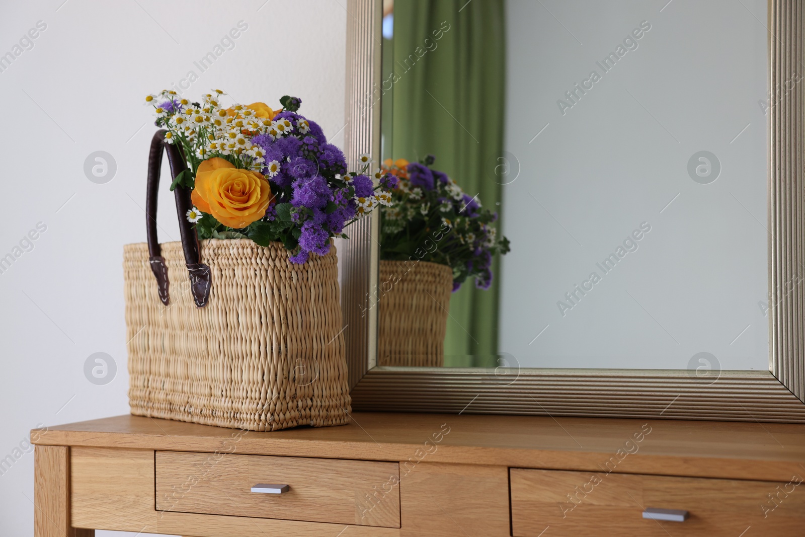 Photo of Wicker basket with beautiful flowers on wooden table indoors, space for text