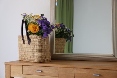 Wicker basket with beautiful flowers on wooden table indoors, space for text