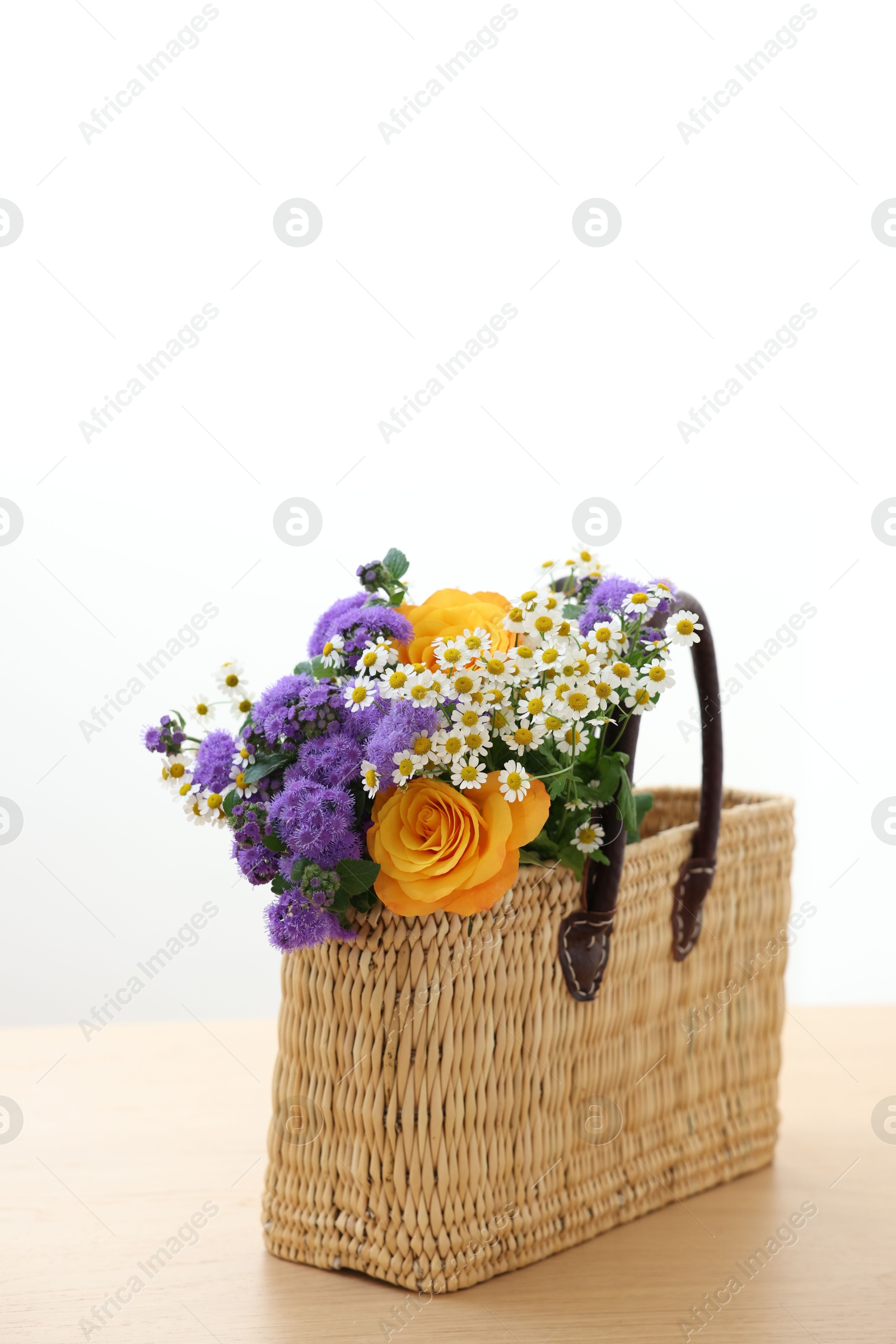 Photo of Wicker basket with beautiful flowers on light wooden table, space for text