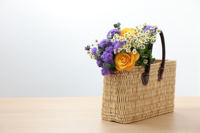 Photo of Wicker basket with beautiful flowers on light wooden table, space for text