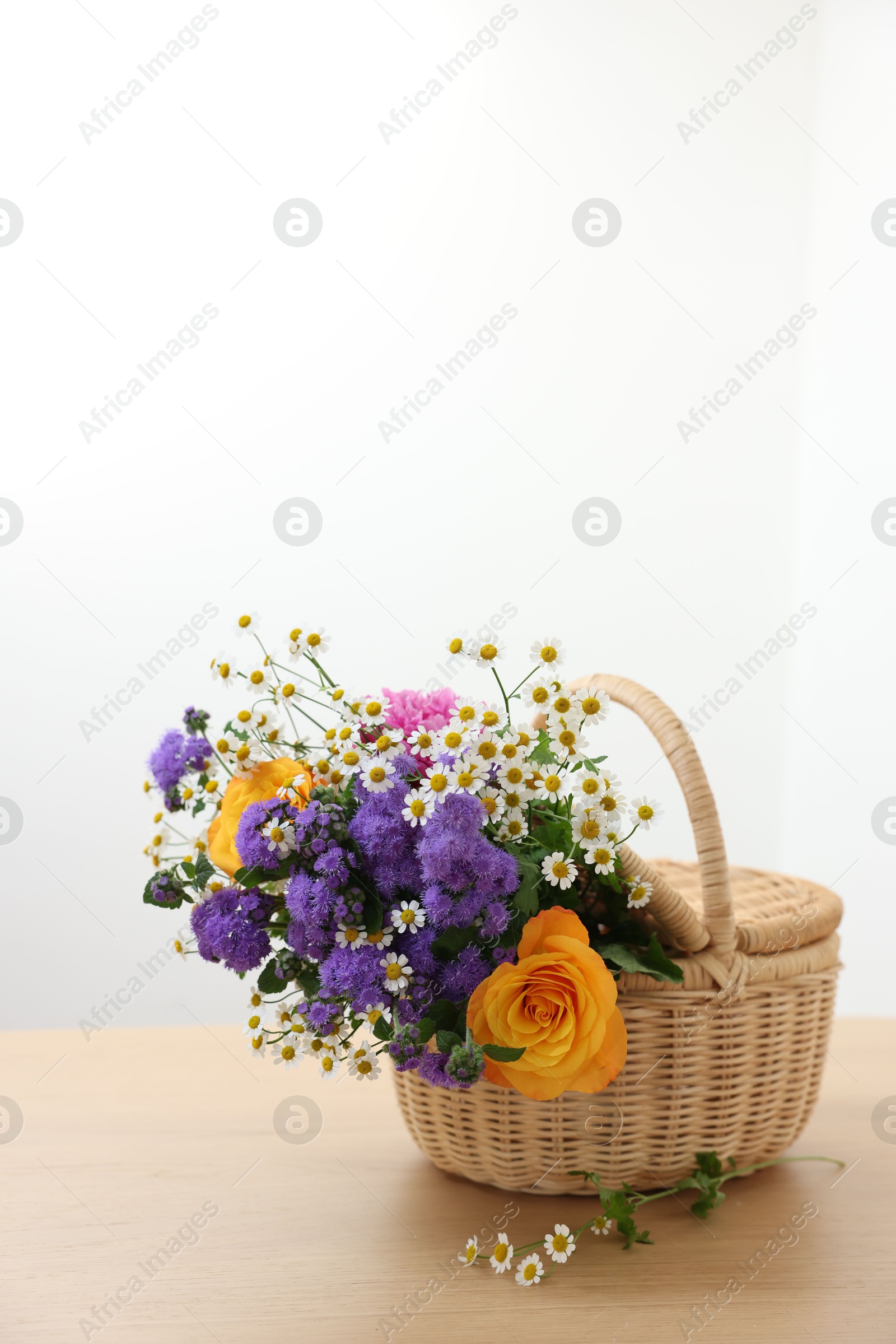 Photo of Wicker basket with beautiful flowers on light wooden table, space for text