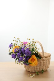 Photo of Wicker basket with beautiful flowers on light wooden table, space for text