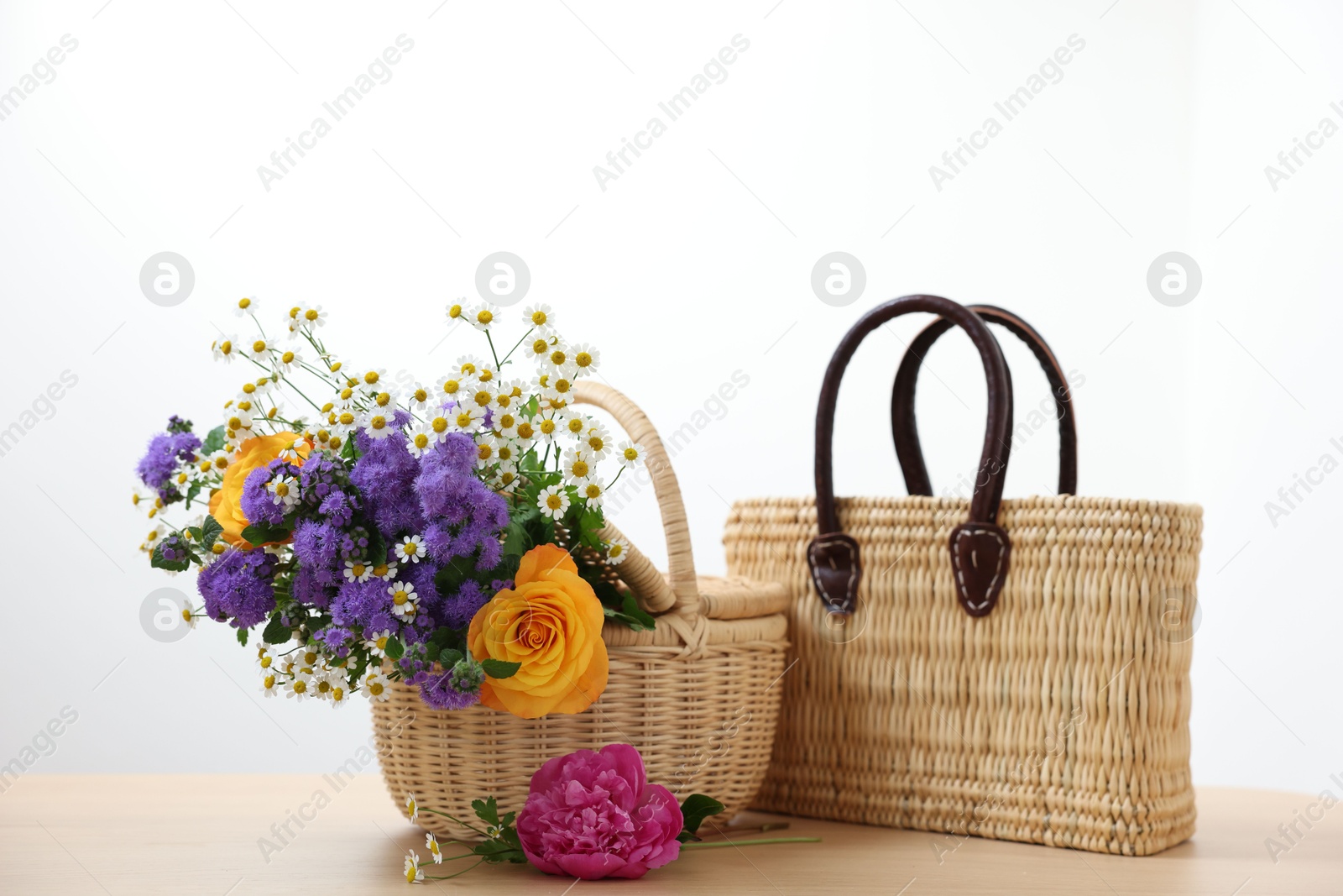 Photo of Wicker baskets and beautiful flowers on light wooden table