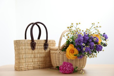 Photo of Wicker baskets and beautiful flowers on light wooden table