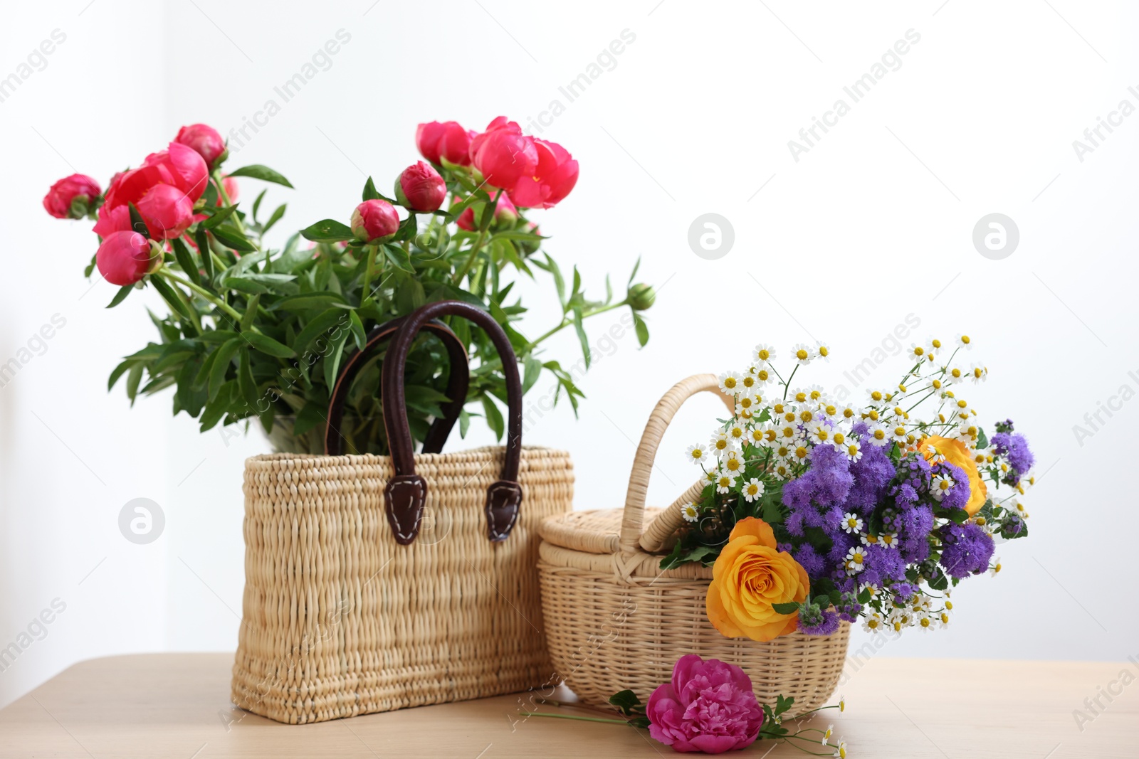 Photo of Wicker baskets with beautiful flowers on light wooden table