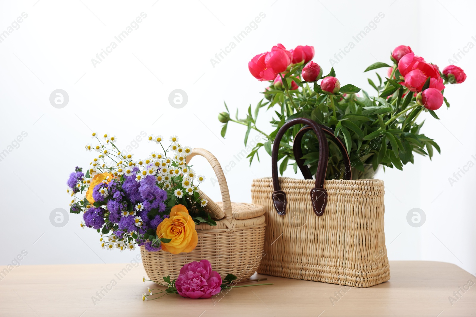 Photo of Wicker baskets with beautiful flowers on light wooden table