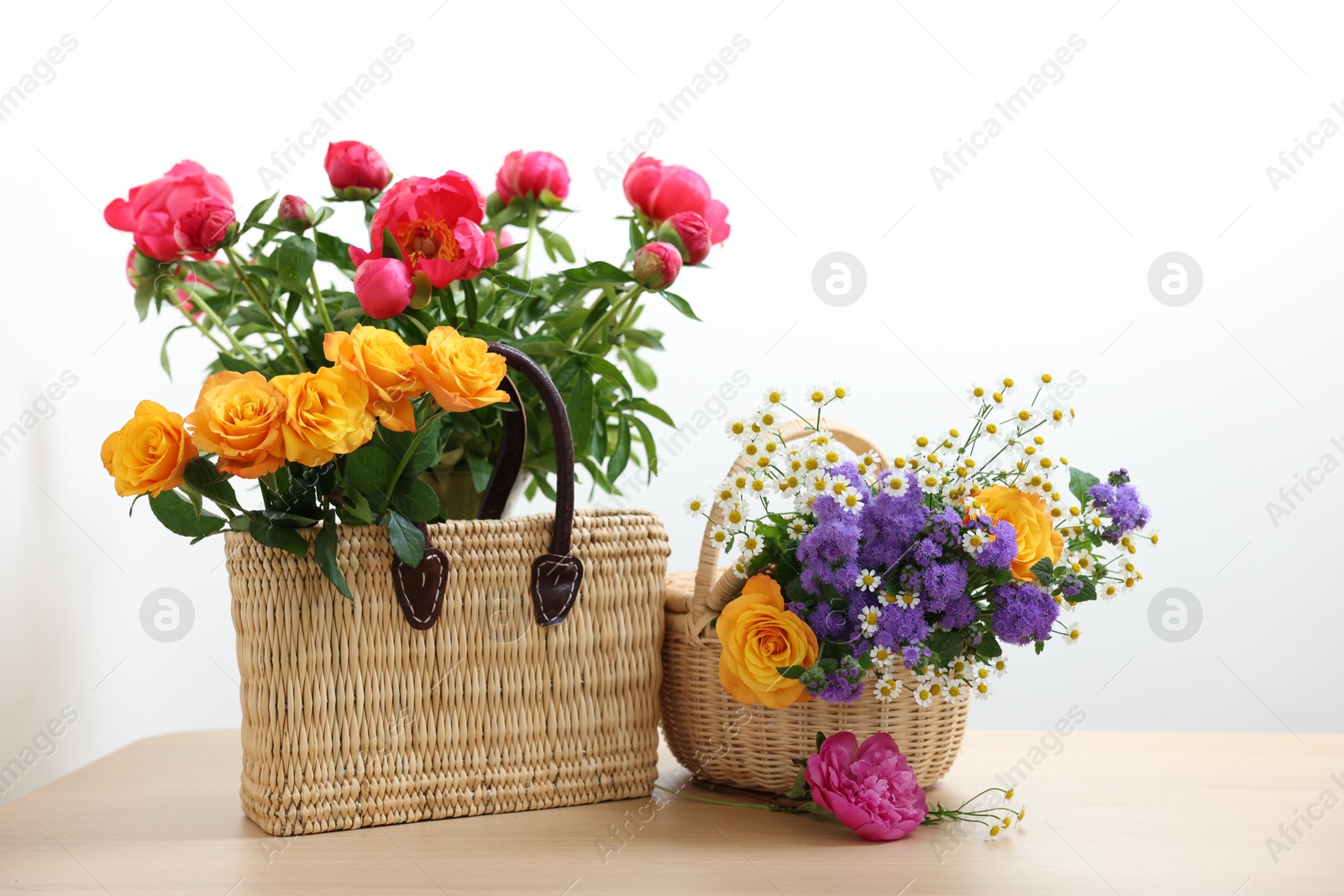 Photo of Wicker baskets with beautiful flowers on light wooden table