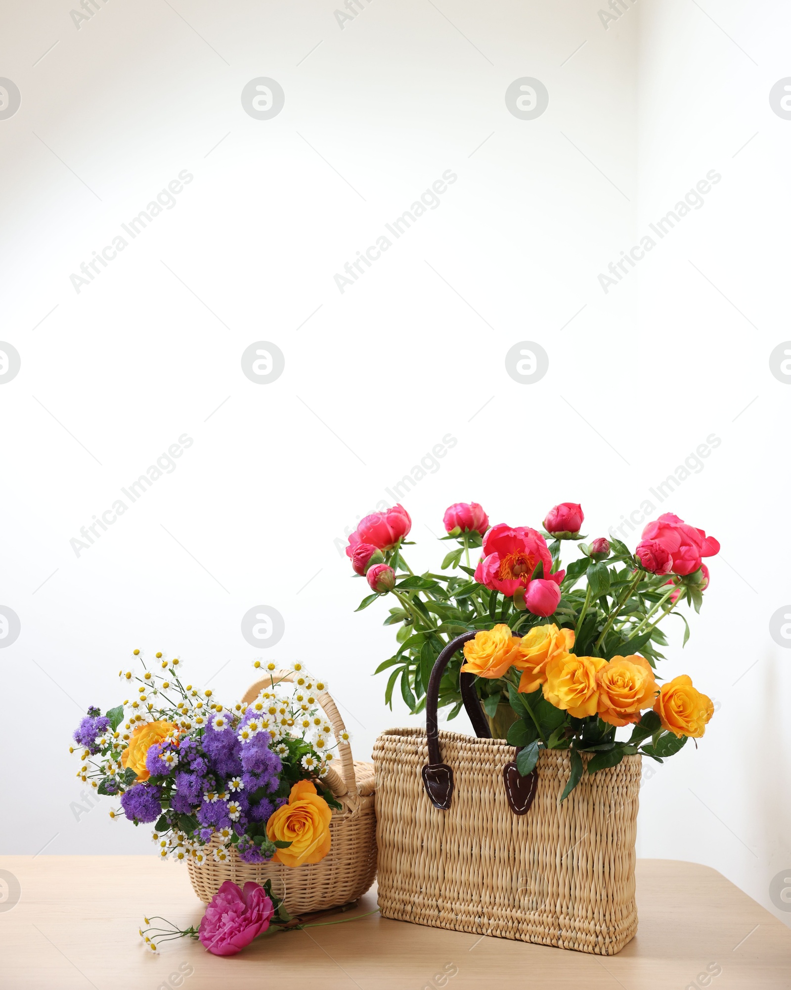 Photo of Wicker baskets with beautiful flowers on light wooden table