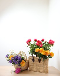 Photo of Wicker baskets with beautiful flowers on light wooden table