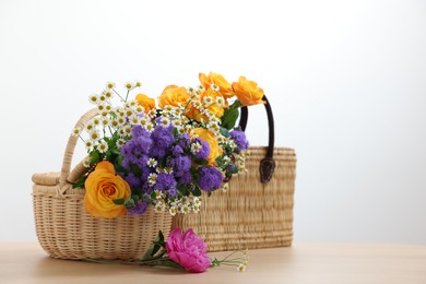 Photo of Wicker baskets with beautiful flowers on light wooden table, space for text