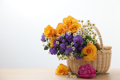 Photo of Wicker basket with beautiful flowers on light wooden table, space for text