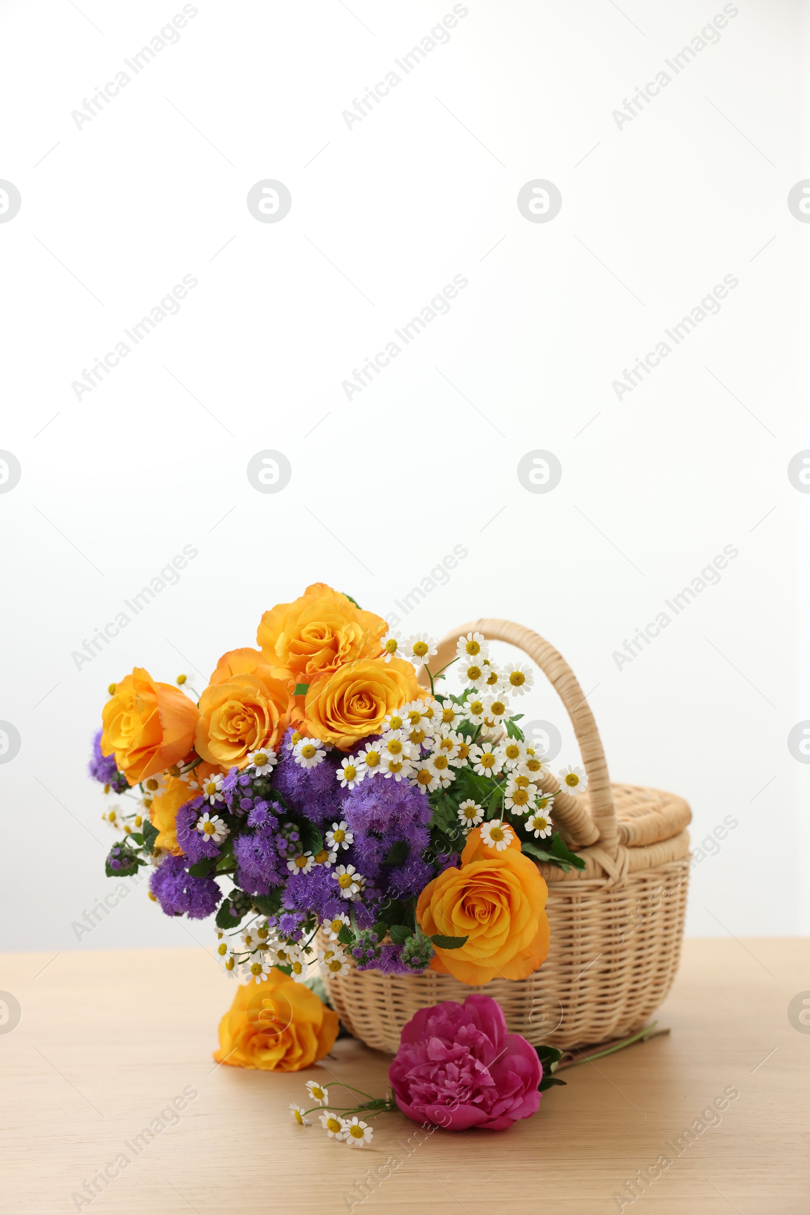 Photo of Wicker basket with beautiful flowers on light wooden table, space for text