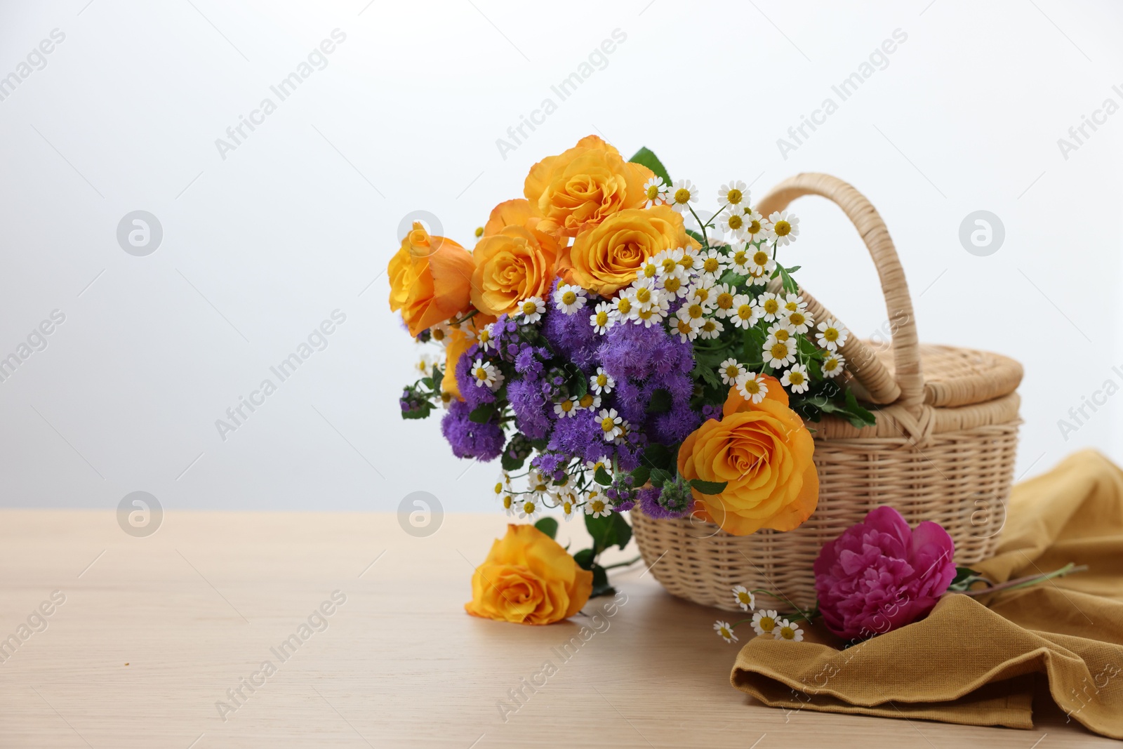 Photo of Wicker basket with beautiful flowers on light wooden table, space for text