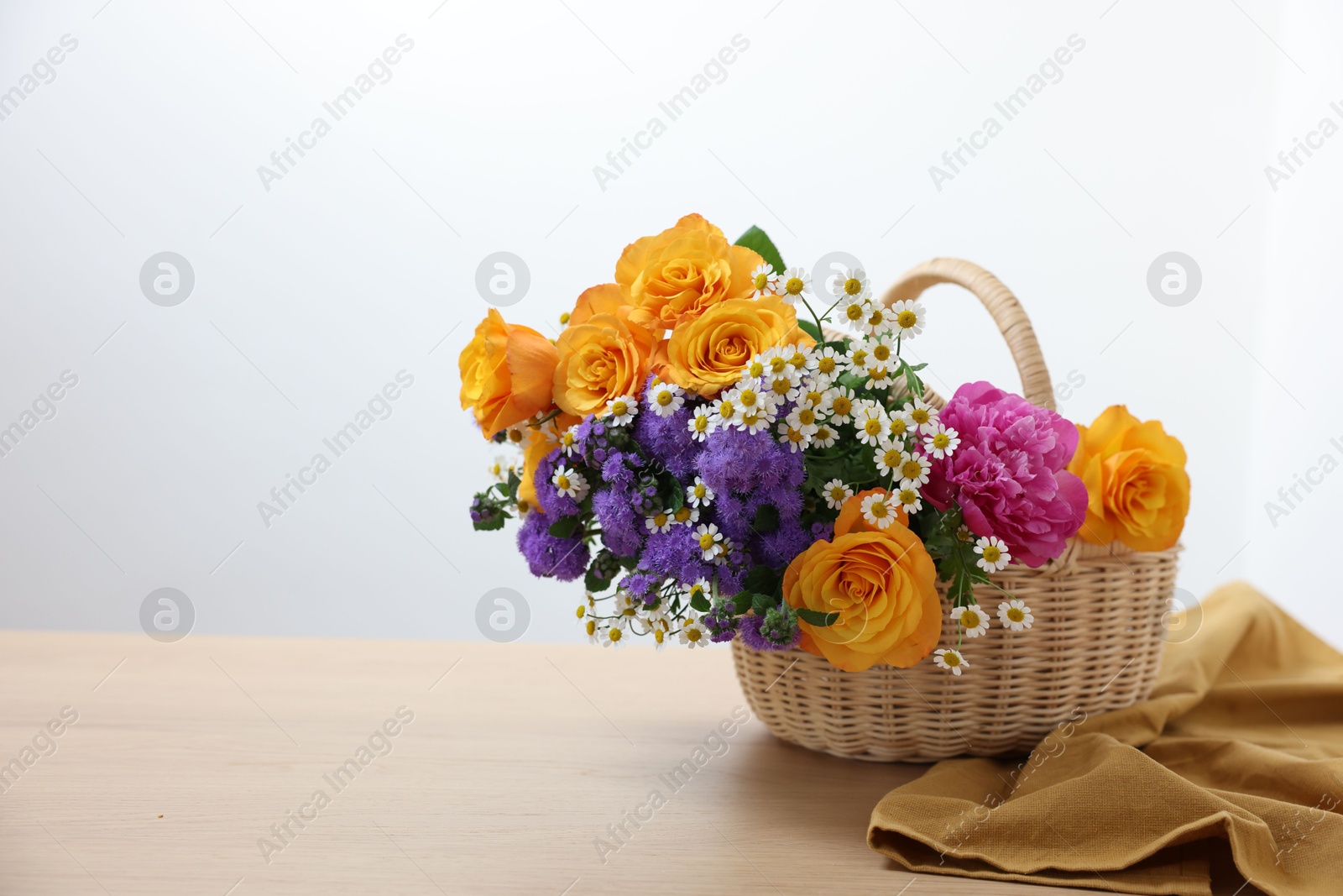 Photo of Wicker basket with beautiful flowers on light wooden table, space for text