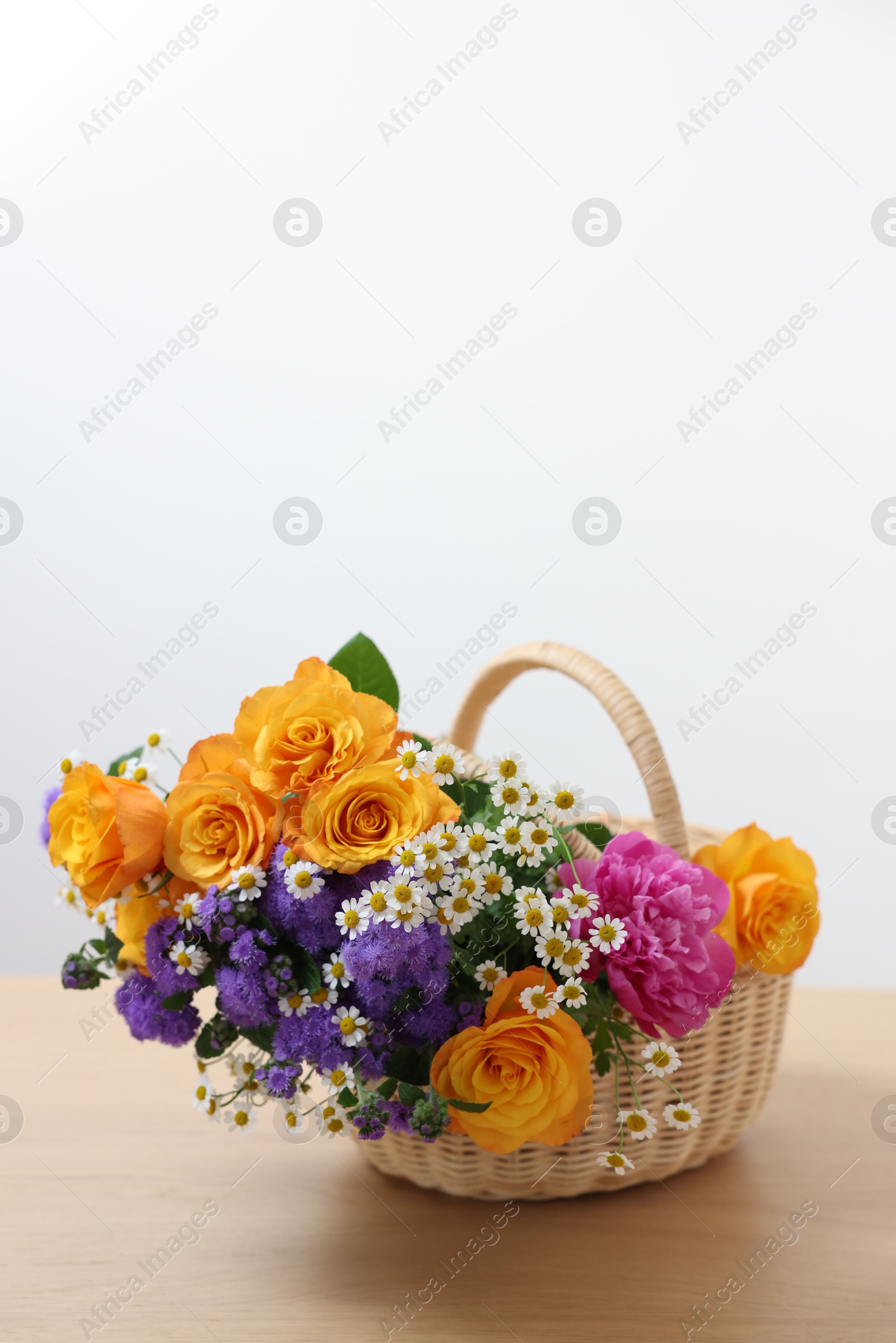 Photo of Wicker basket with beautiful flowers on light wooden table, space for text