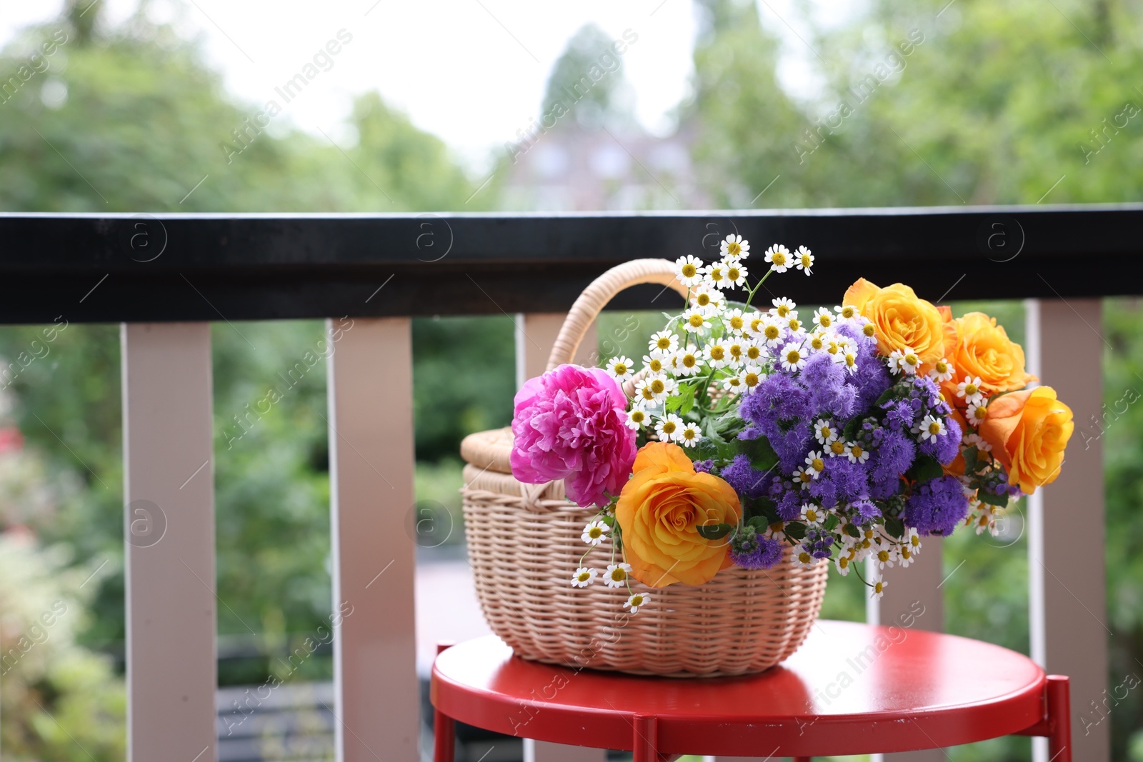 Photo of Wicker basket with beautiful flowers on red table at balcony, space for text