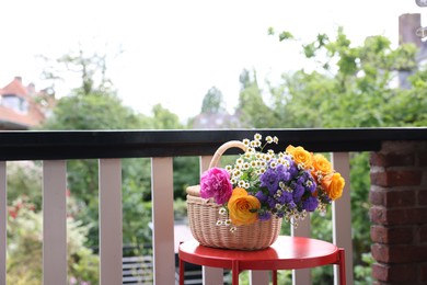 Photo of Wicker basket with beautiful flowers on red table at balcony, space for text