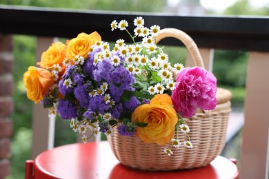 Photo of Wicker basket with beautiful flowers on red table at balcony