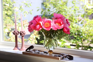 Photo of Beautiful pink peonies in vase, decorative stones and candles on windowsill