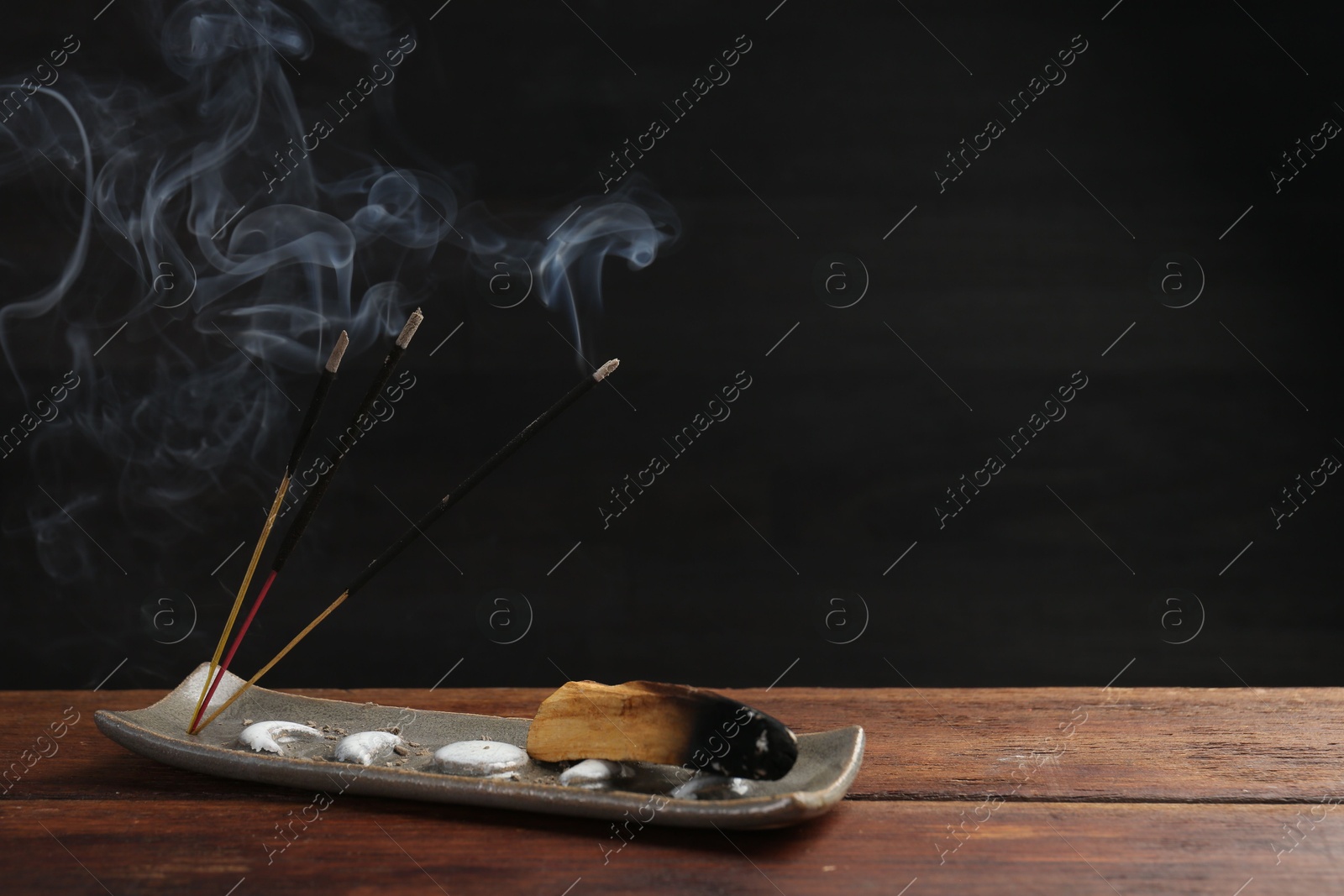 Photo of Aromatic incense sticks smoldering on wooden table. Space for text