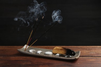 Photo of Aromatic incense sticks smoldering on wooden table. Space for text