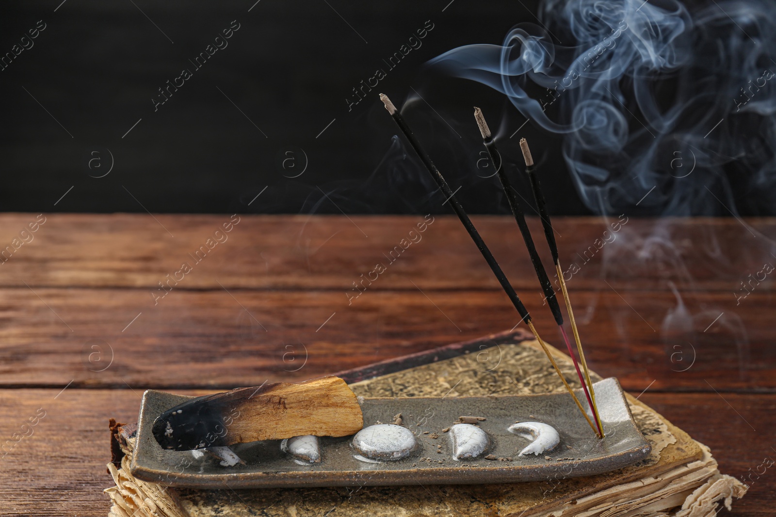 Photo of Aromatic incense sticks smoldering on wooden table, closeup. Space for text